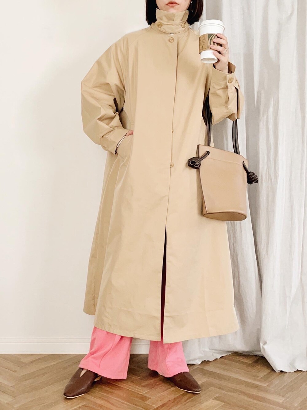 ベージュ系のステンカラーコート、ブラウン系のショルダーバッグ、ピンク系のその他パンツを着用したレディースの春コーディネートの2枚目の写真