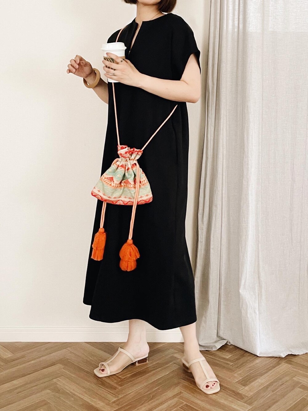ブラック系のワンピース、ブラック系のサンダル、オレンジ系のショルダーバッグを着用したレディースの夏コーディネートの2枚目の写真