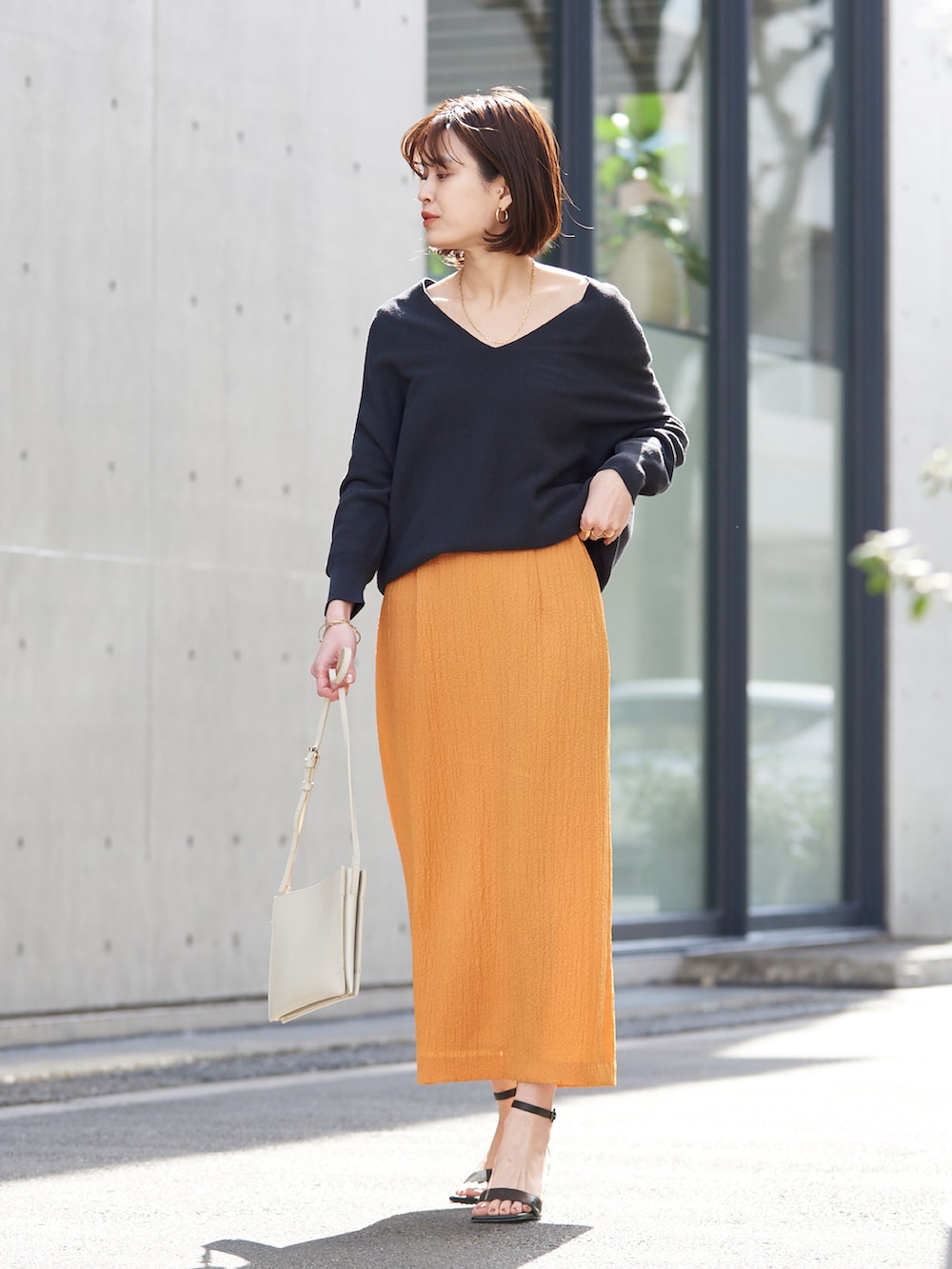 オレンジ系のスカート、グレー系のニット/セーターを着用したレディースの春コーディネートの2枚目の写真