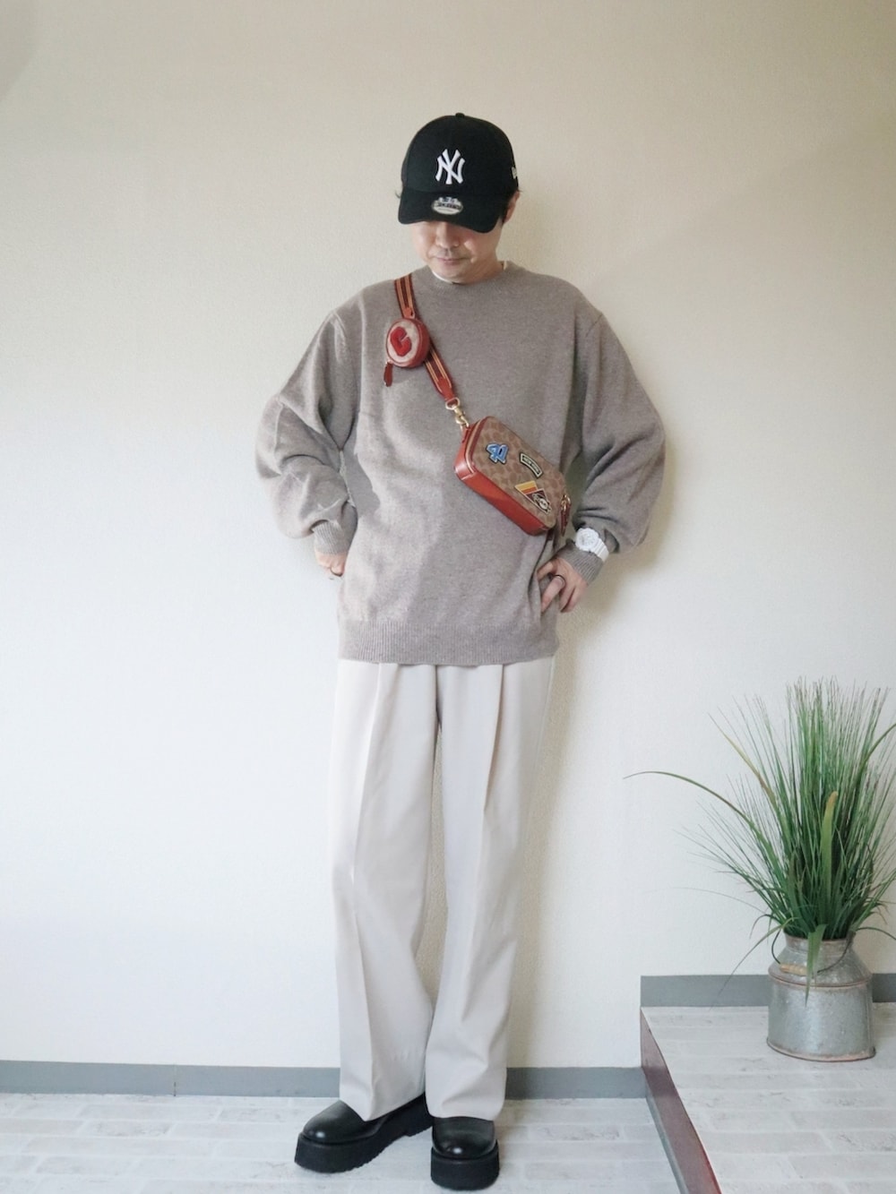 ベージュ系のニット/セーター、ブラウン系のショルダーバッグ、ブラック系のドレスシューズを着用したメンズの秋コーディネートの2枚目の写真