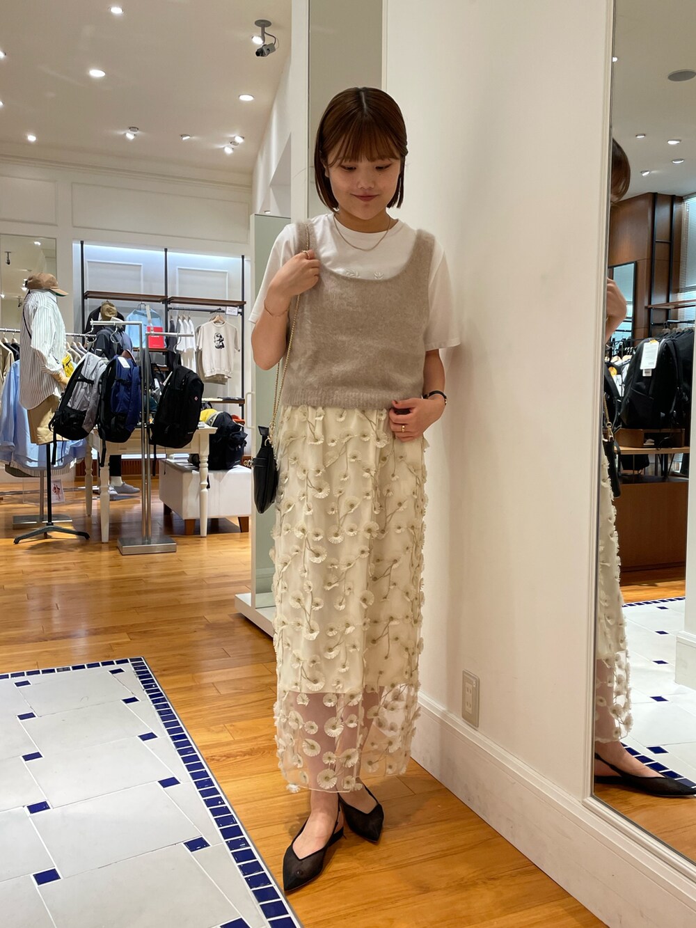 イエロー系のベスト、ホワイト系のスカート、ブラック系のショルダーバッグを着用したレディースの秋コーディネートの2枚目の写真