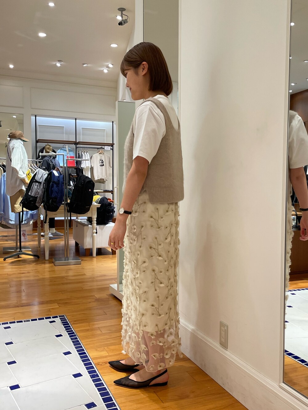 イエロー系のベスト、ホワイト系のスカート、ブラック系のショルダーバッグを着用したレディースの秋コーディネートの3枚目の写真