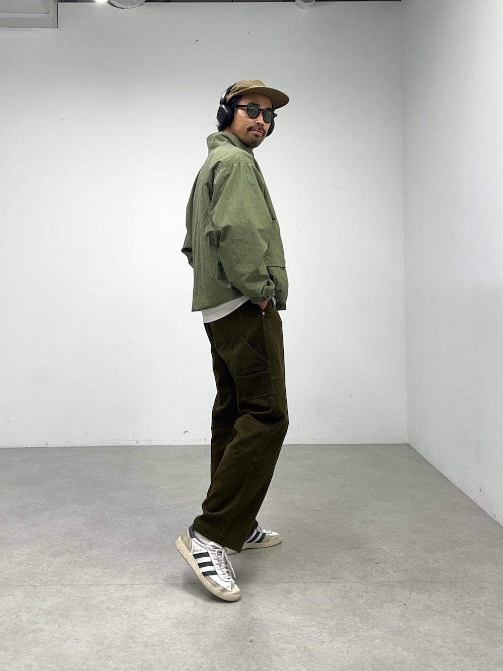 グリーン系のナイロンジャケット、グレー系のパンツ、ブラウン系のキャップを着用したメンズの夏コーディネートの2枚目の写真