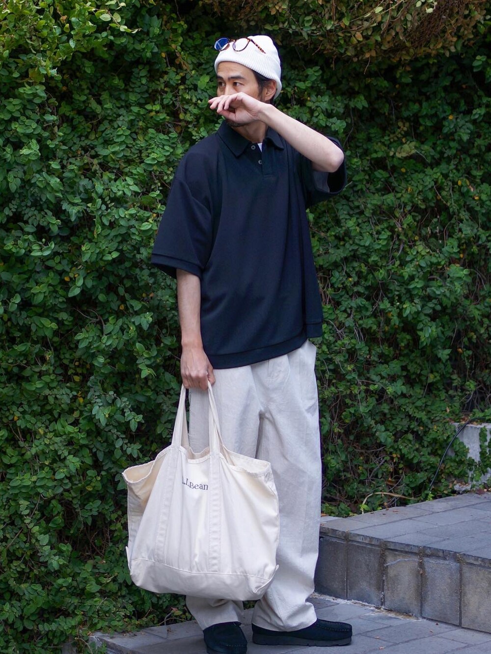ブラック系のポロシャツ、ブラック系のブーツ、ホワイト系のトートバッグを着用したメンズの春コーディネートの2枚目の写真