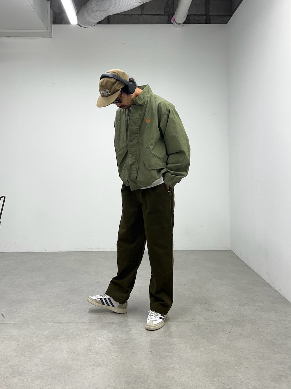 グリーン系のナイロンジャケット、グレー系のパンツ、ブラウン系のキャップを着用したメンズの夏コーディネートの3枚目の写真