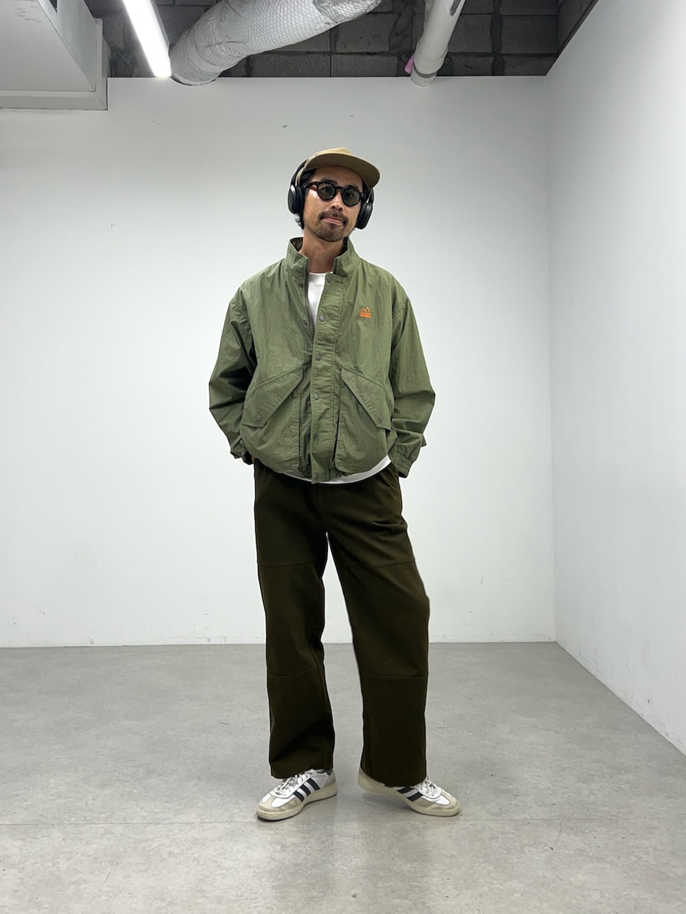 グリーン系のナイロンジャケット、グレー系のパンツ、ブラウン系のキャップを着用したメンズの夏コーディネートの4枚目の写真