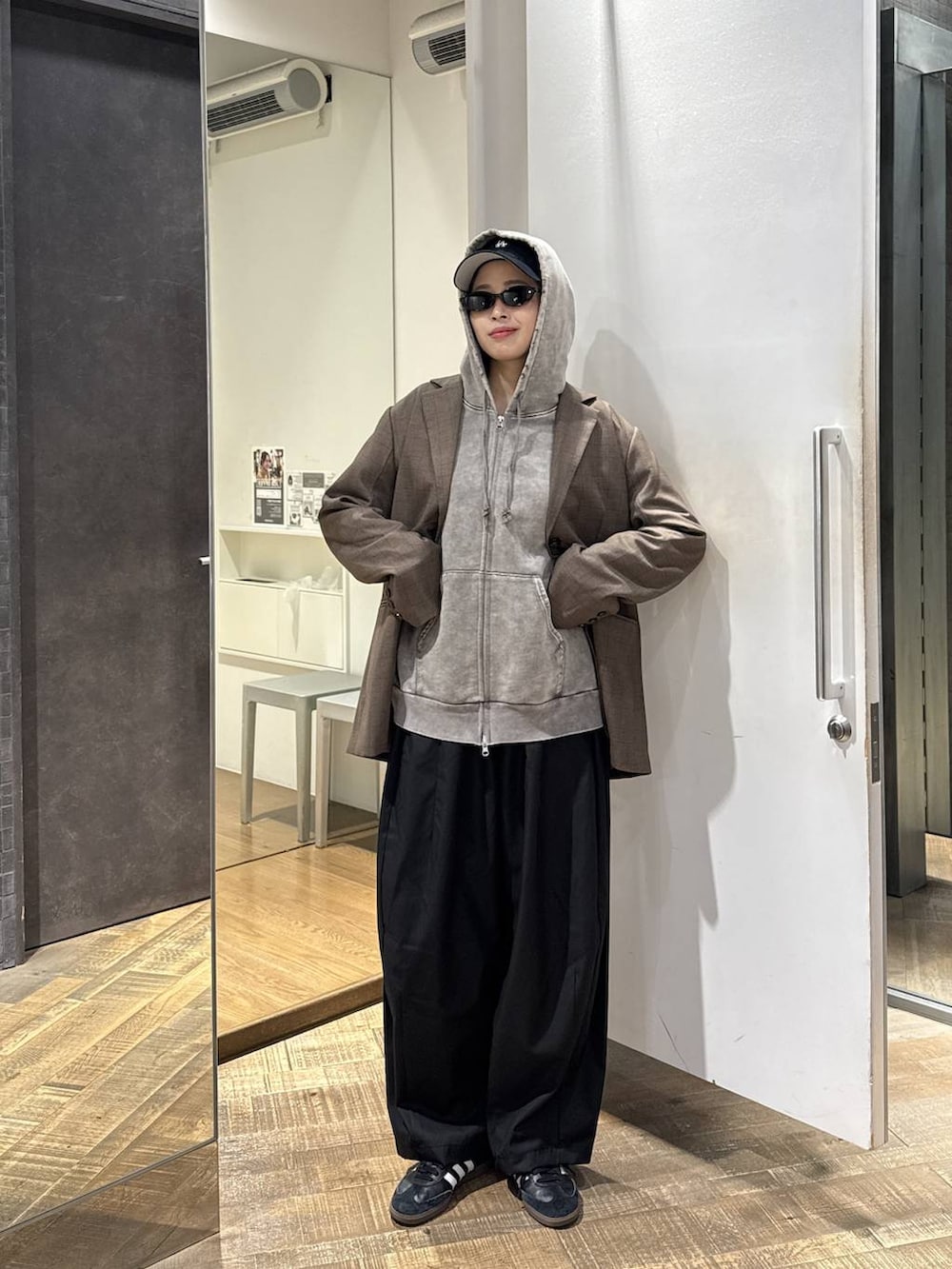 グレー系のパーカー、ブラック系のスラックス、ブラウン系のテーラードジャケットを着用したレディースの秋コーディネートの2枚目の写真