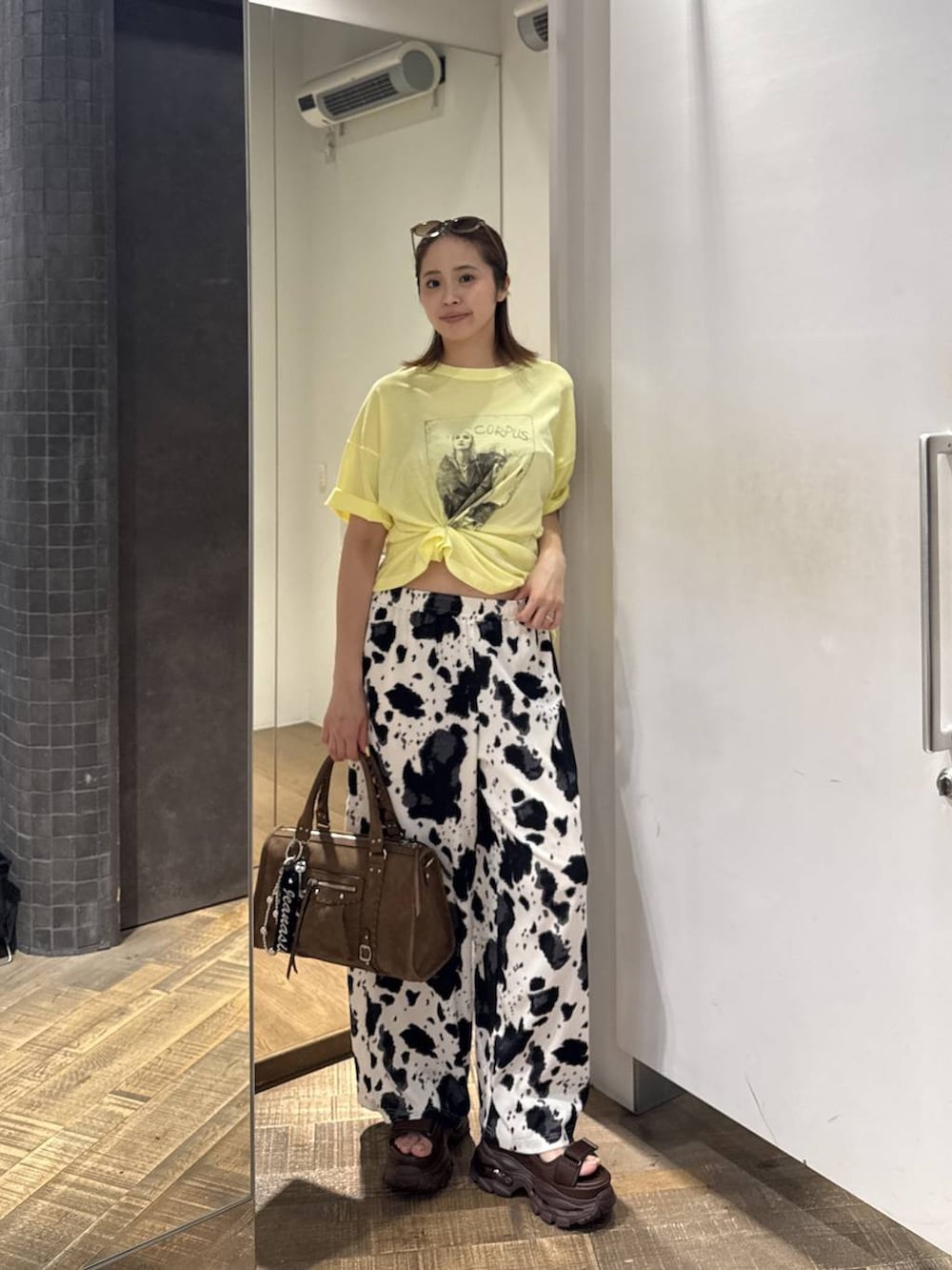 ブラウン系のボストンバッグ、ブラウン系のサンダル、イエロー系のTシャツ/カットソーを着用したレディースの夏コーディネートの3枚目の写真