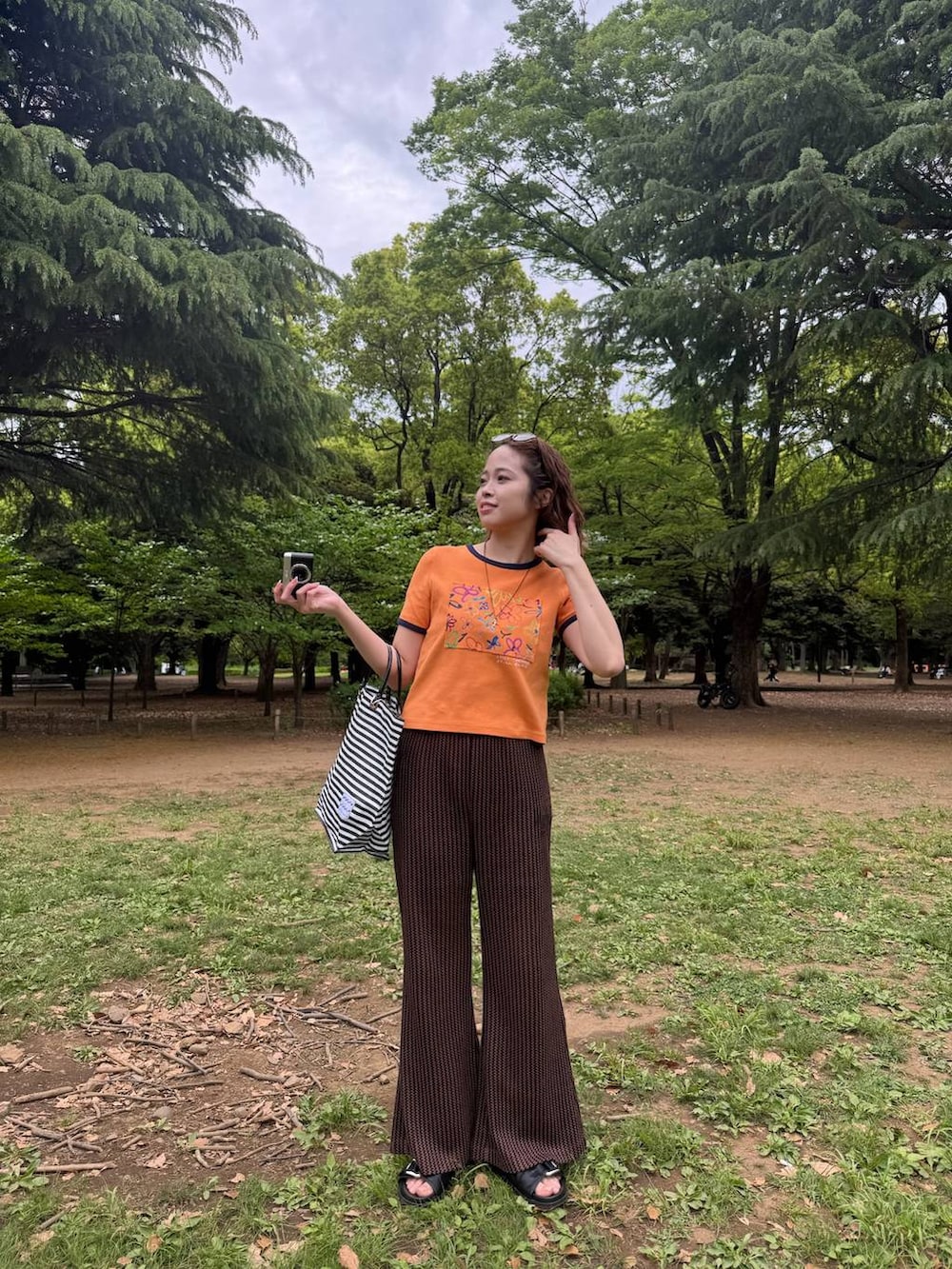 オレンジ系のTシャツ/カットソー、ブラウン系のその他パンツ、ブラック系のサンダルを着用したレディースの夏コーディネートの2枚目の写真