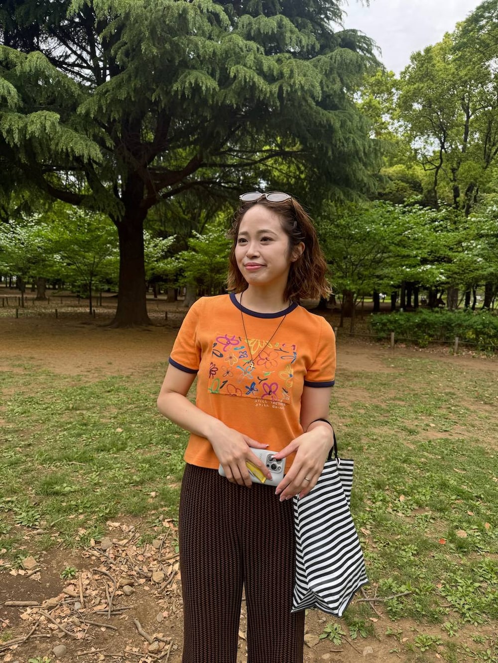 オレンジ系のTシャツ/カットソー、ブラウン系のその他パンツ、ブラック系のサンダルを着用したレディースの夏コーディネートの3枚目の写真