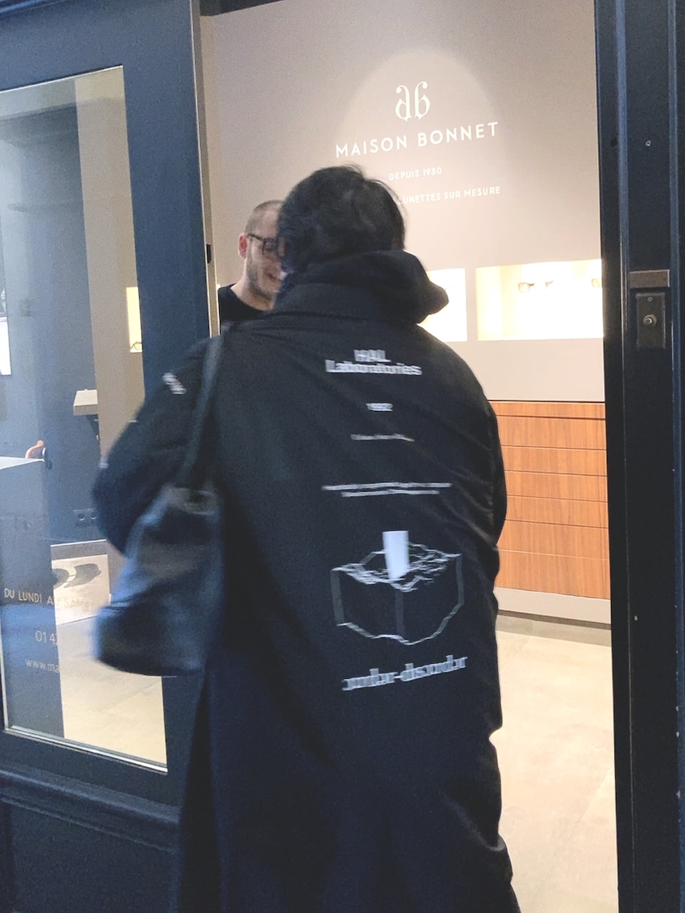 ブラック系のステンカラーコート、ホワイト系のスニーカー、ブラック系のストール/ショールを着用したメンズの秋コーディネートの3枚目の写真