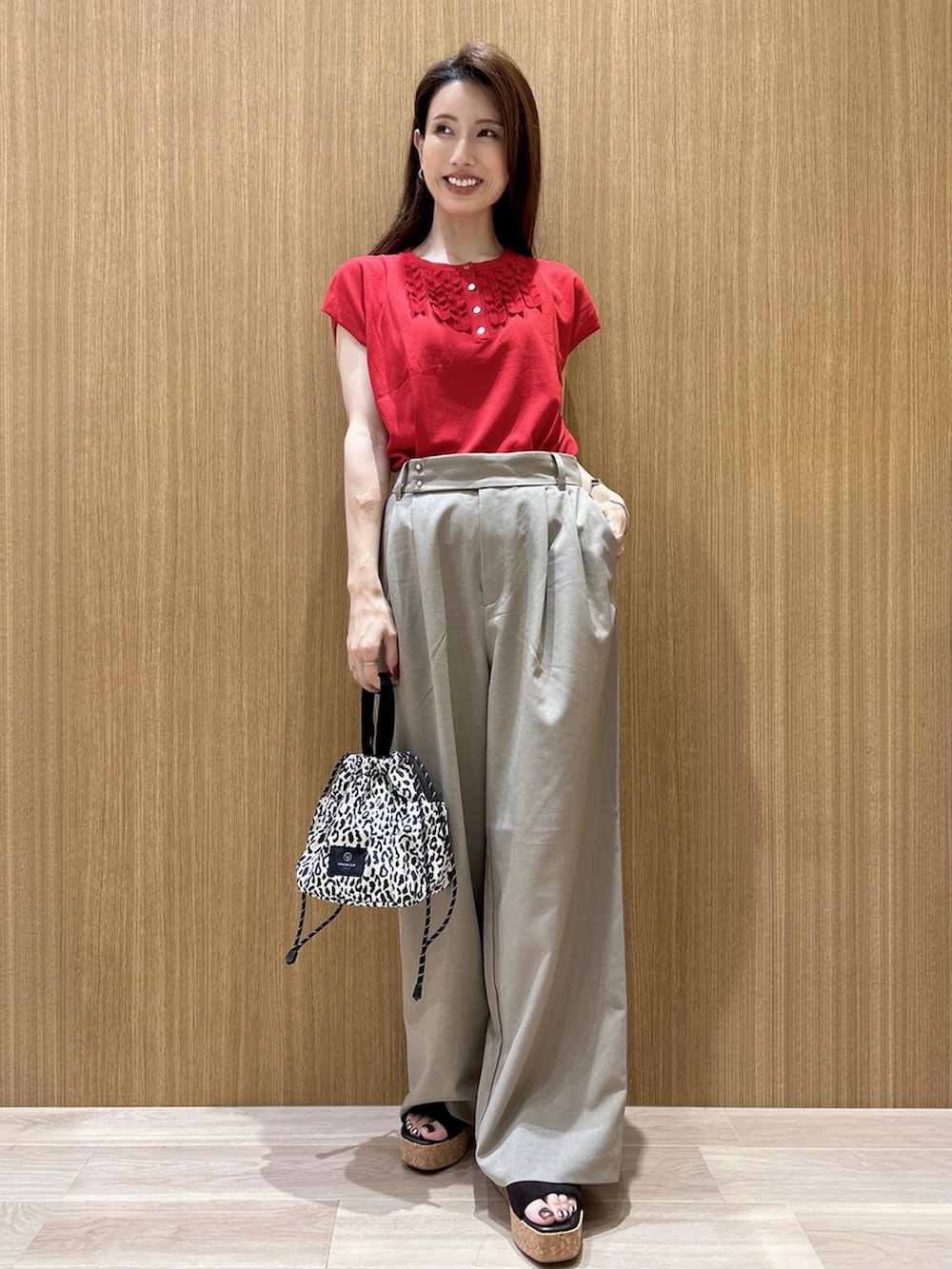レッド系のニット/セーター、ブラウン系のその他パンツ、ベージュ系のショルダーバッグを着用したレディースの夏コーディネートの2枚目の写真