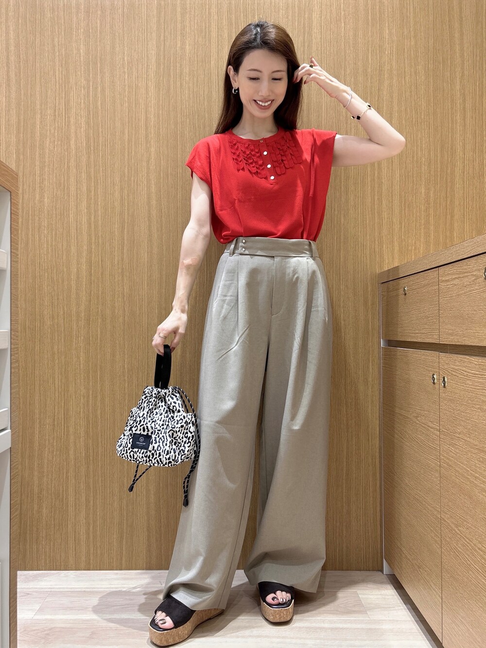 レッド系のニット/セーター、ブラウン系のその他パンツ、ベージュ系のショルダーバッグを着用したレディースの夏コーディネートの3枚目の写真