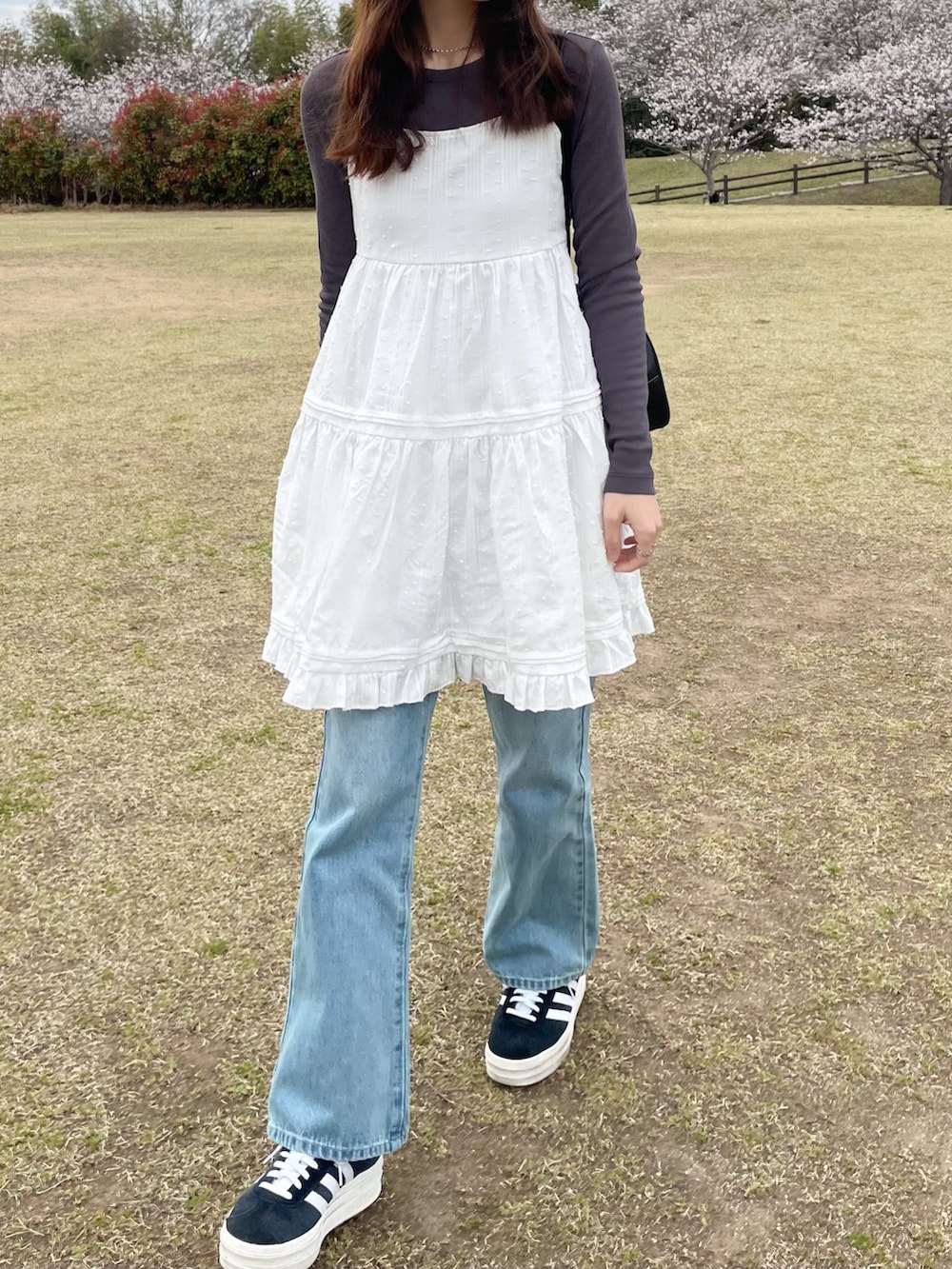 ホワイト系のワンピース、ブルー系のデニムパンツ、ブラック系のスニーカーを着用したレディースの春コーディネートの2枚目の写真