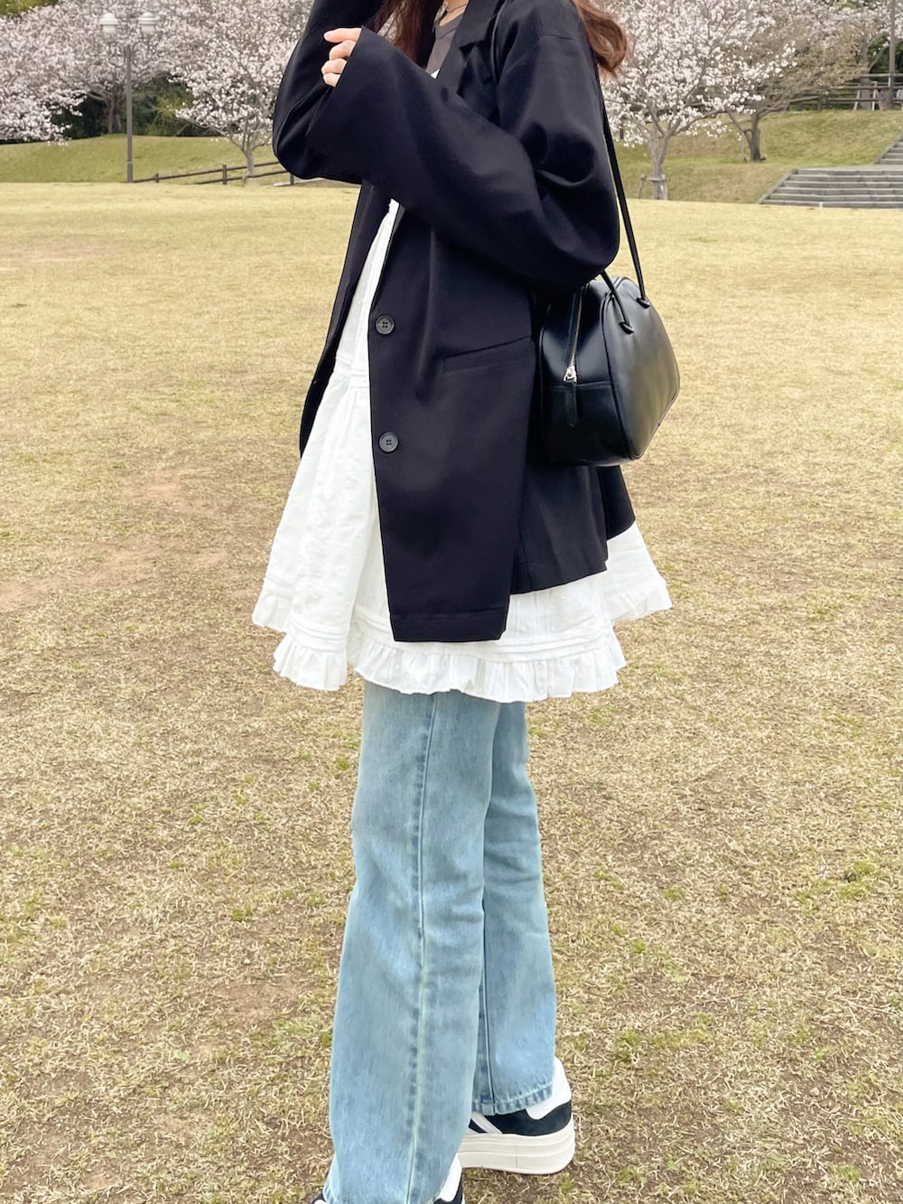 ホワイト系のワンピース、ブルー系のデニムパンツ、ブラック系のスニーカーを着用したレディースの春コーディネートの3枚目の写真