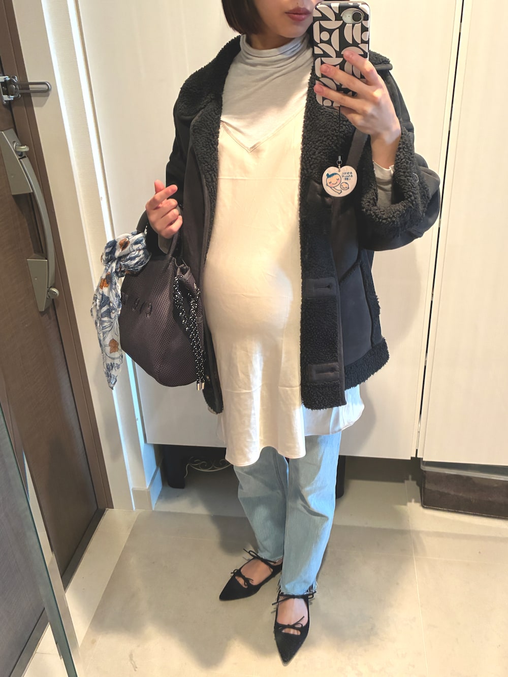 ブルー系のデニムパンツ、グレー系のショルダーバッグ、ブラック系のムートンコートを着用したレディースの春コーディネートの2枚目の写真