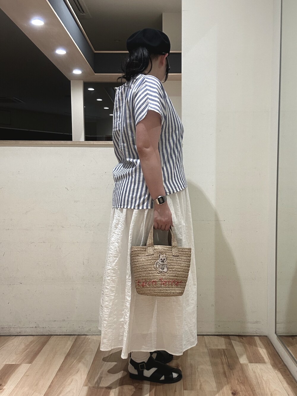 ブラック系のサンダル、ブラウン系のハンドバッグ、ホワイト系のスカートを着用したレディースの春コーディネートの2枚目の写真