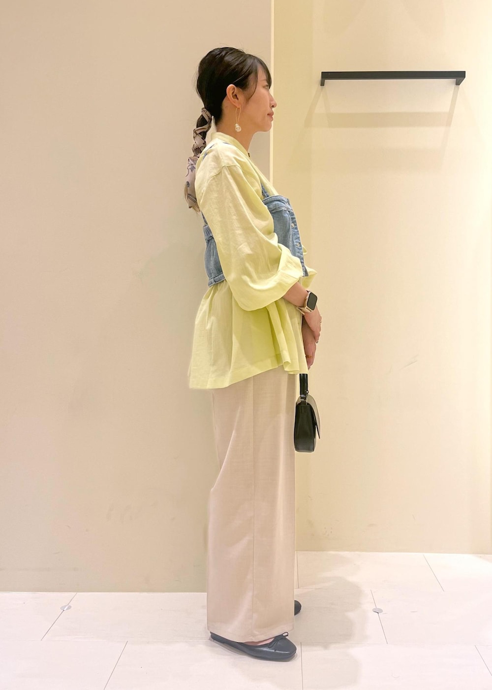 ブラック系のハンドバッグ、ブルー系のベスト、イエロー系のシャツ/ブラウスを着用したレディースの春コーディネートの4枚目の写真