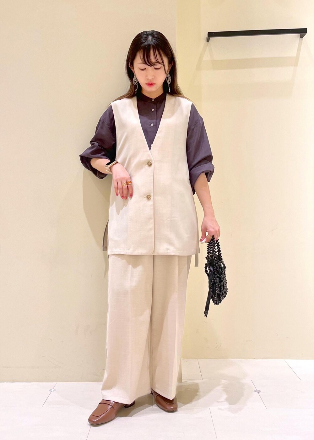 イエロー系のローファー、ブラック系のハンドバッグ、ベージュ系のベストを着用したレディースの春コーディネートの2枚目の写真