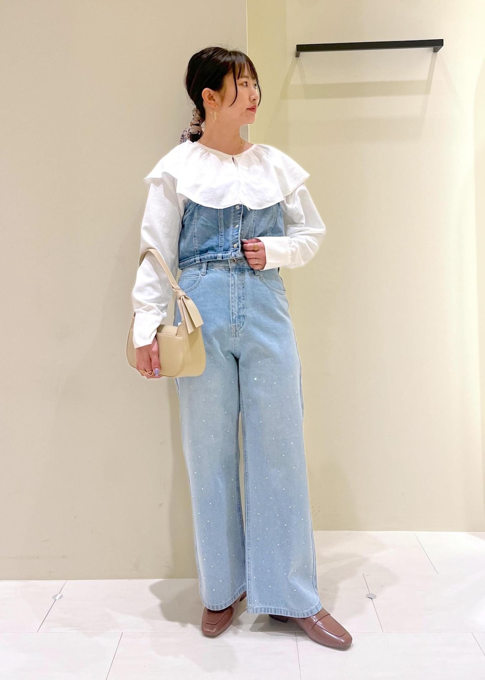 ベージュ系のハンドバッグ、ブルー系のデニムパンツ、ブルー系のベストを着用したレディースの春コーディネートの2枚目の写真