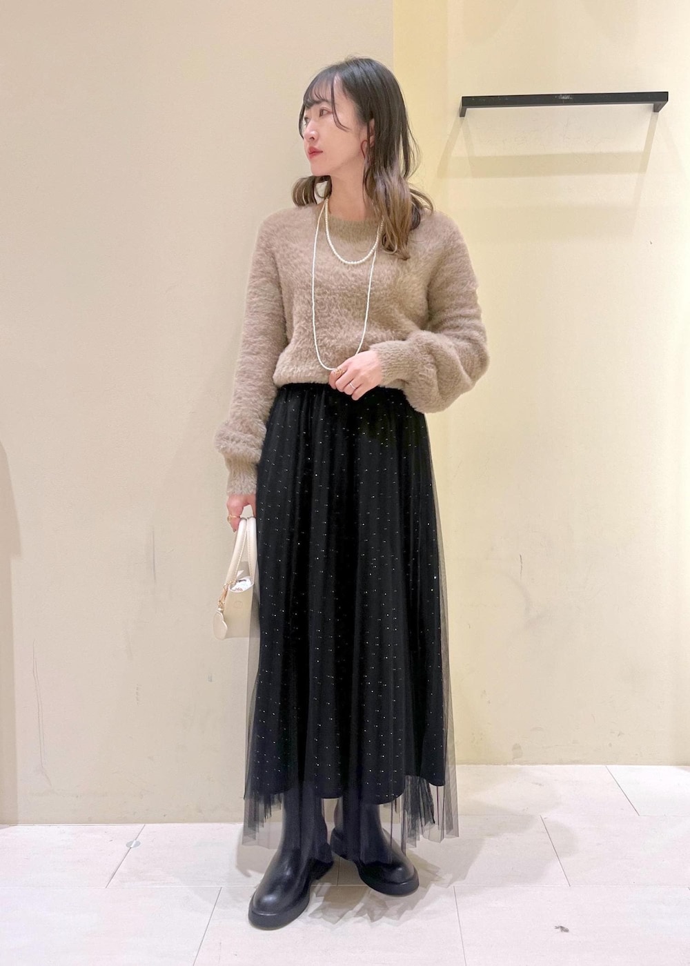 ホワイト系のショルダーバッグ、ブラック系のブーツ、ブラック系のスカートを着用したレディースの冬コーディネートの2枚目の写真