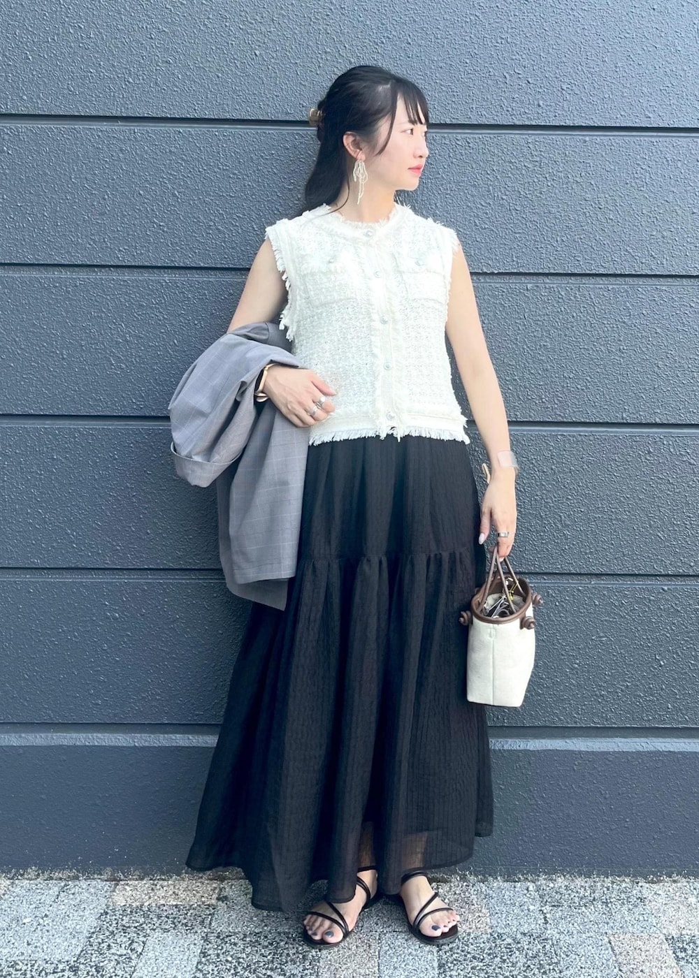 グレー系のテーラードジャケット、ブラウン系のトートバッグ、ブラック系のスカートを着用したレディースの夏コーディネートの2枚目の写真