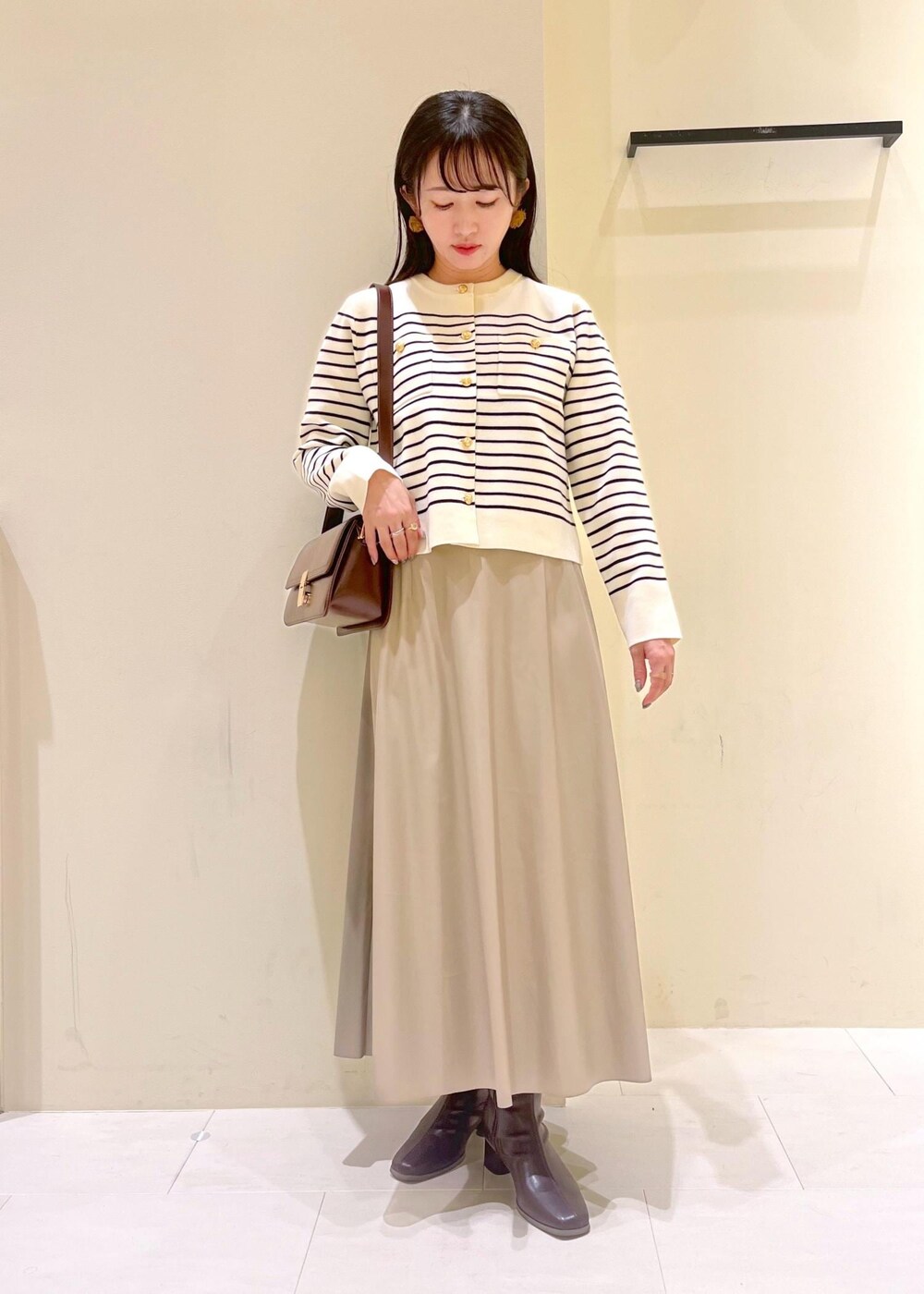 レッド系のショルダーバッグ、ベージュ系のスカート、ホワイト系のカーディガン/ボレロを着用したレディースの秋コーディネートの2枚目の写真