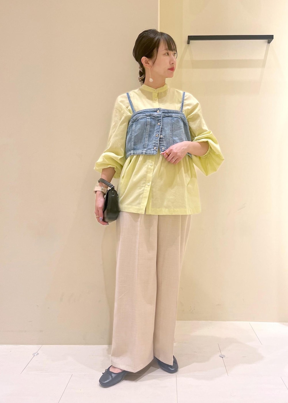 ブラック系のハンドバッグ、ブルー系のベスト、イエロー系のシャツ/ブラウスを着用したレディースの春コーディネートの2枚目の写真