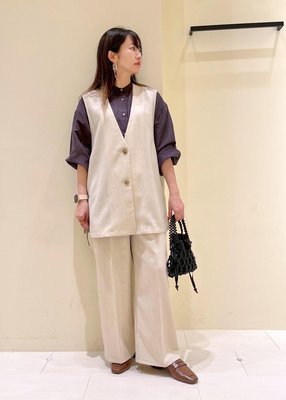 イエロー系のローファー、ブラック系のハンドバッグ、ベージュ系のベストを着用したレディースの春コーディネートの3枚目の写真