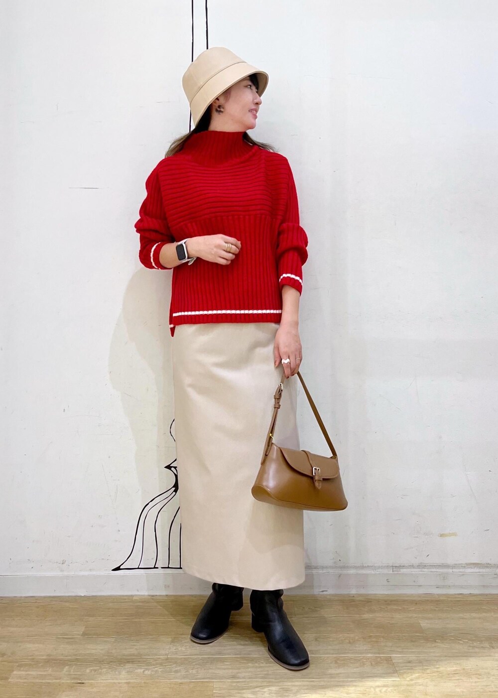 ベージュ系のスカート、レッド系のニット/セーター、ブラック系のブーツを着用したレディースの秋コーディネートの3枚目の写真