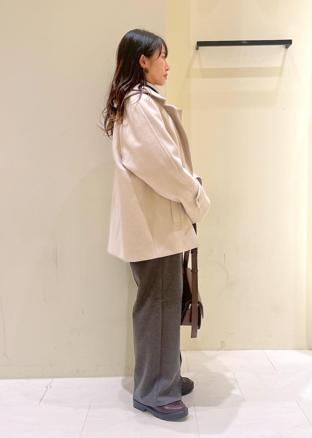 レッド系のショルダーバッグ、ホワイト系のニット/セーター、ベージュ系のその他アウターを着用したレディースの冬コーディネートの2枚目の写真