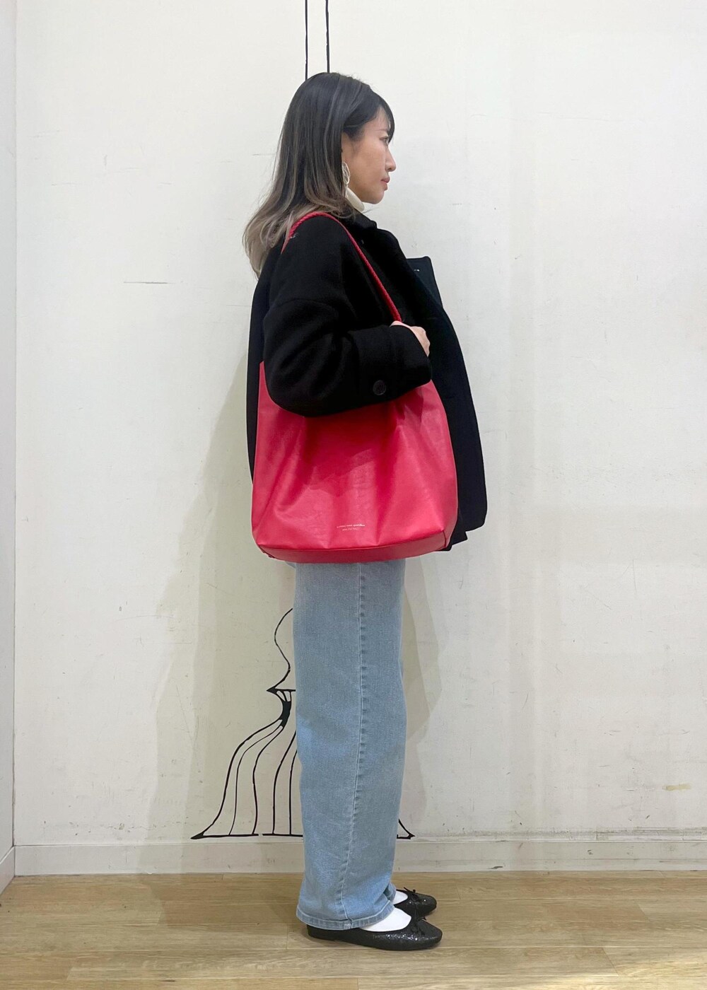 ブルー系のデニムパンツ、レッド系のトートバッグ、ブラック系のその他アウターを着用したレディースの冬コーディネートの2枚目の写真