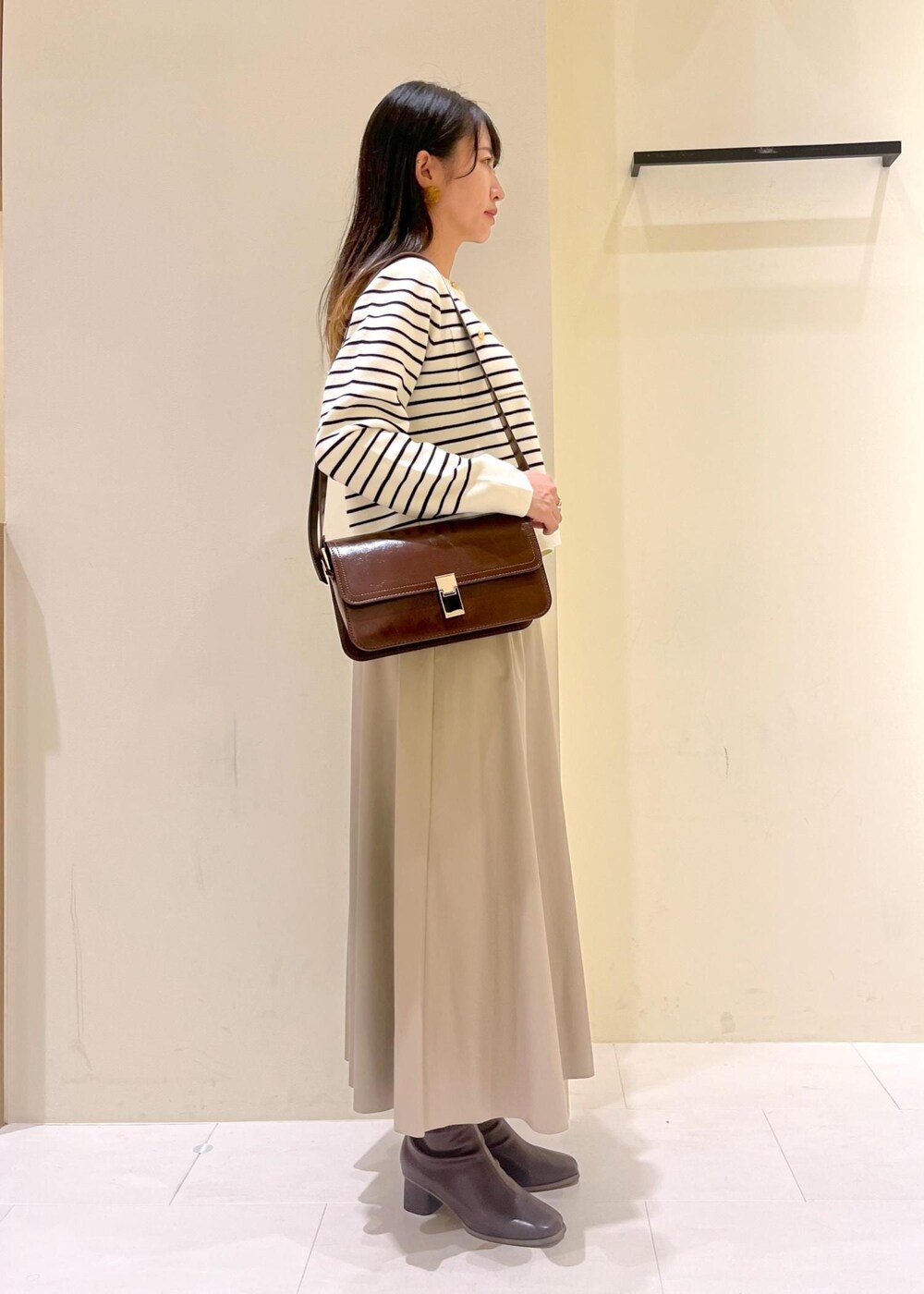 レッド系のショルダーバッグ、ベージュ系のスカート、ホワイト系のカーディガン/ボレロを着用したレディースの秋コーディネートの3枚目の写真