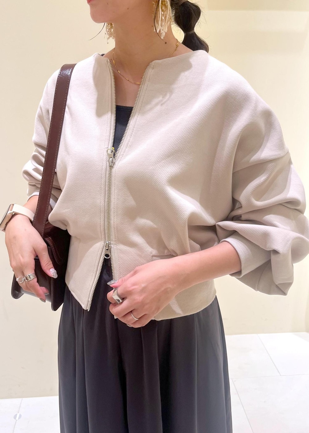 レッド系のショルダーバッグ、ベージュ系のパンプス、ベージュ系のカーディガン/ボレロを着用したレディースの秋コーディネートの6枚目の写真