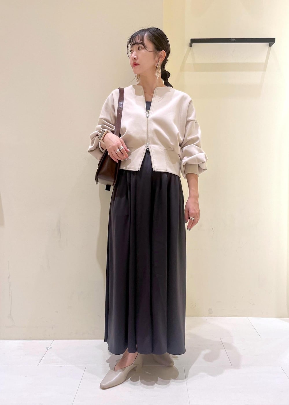 レッド系のショルダーバッグ、ベージュ系のパンプス、ベージュ系のカーディガン/ボレロを着用したレディースの秋コーディネートの2枚目の写真