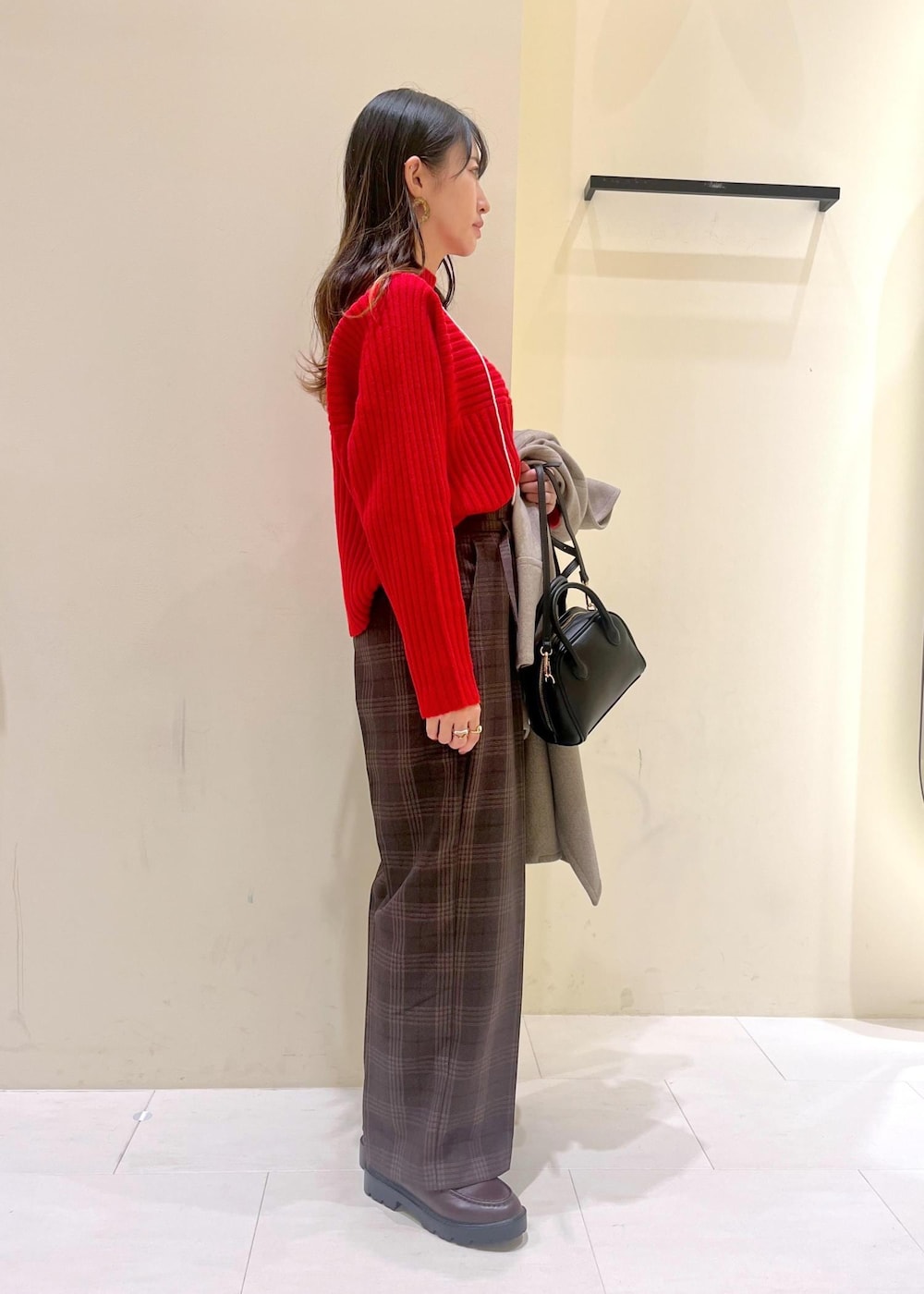 ブラック系のショルダーバッグ、レッド系のニット/セーター、ブラウン系のピーコートを着用したレディースの冬コーディネートの2枚目の写真