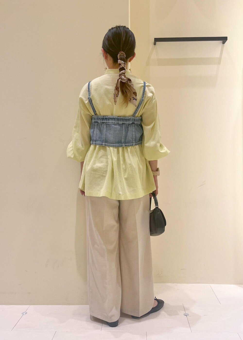 ブラック系のハンドバッグ、ブルー系のベスト、イエロー系のシャツ/ブラウスを着用したレディースの春コーディネートの5枚目の写真