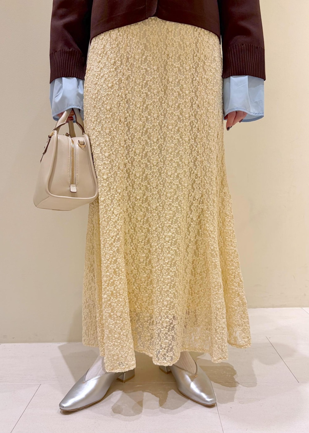 ホワイト系のボストンバッグ、ベージュ系のスカート、ブラウン系のカーディガン/ボレロを着用したレディースの春コーディネートの6枚目の写真