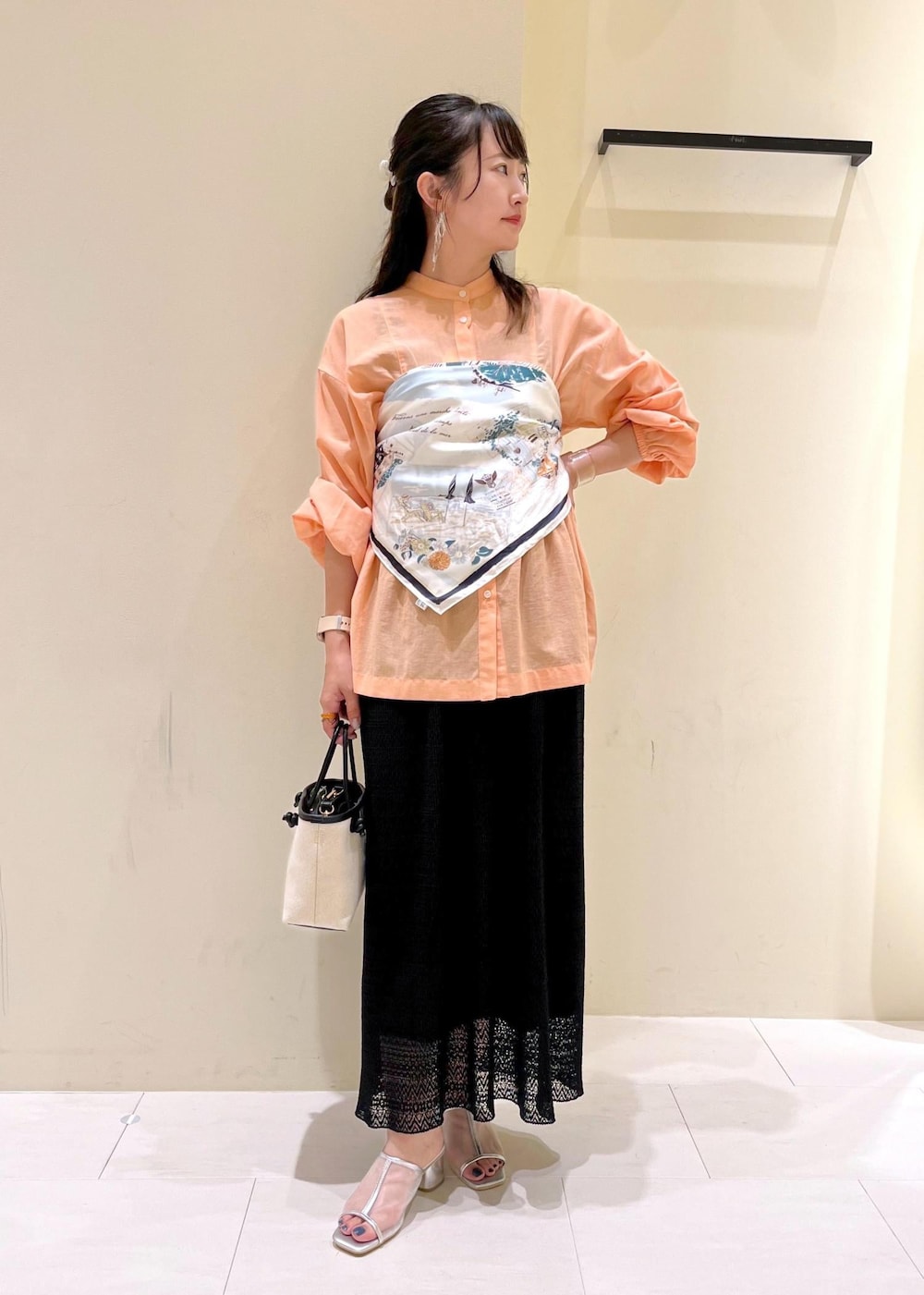 オレンジ系のシャツ/ブラウス、シルバー系のパンプス、ブラック系のトートバッグを着用したレディースの夏コーディネートの2枚目の写真