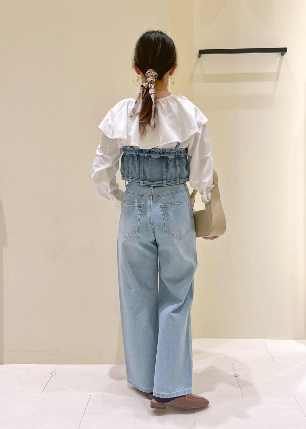 ベージュ系のハンドバッグ、ブルー系のデニムパンツ、ブルー系のベストを着用したレディースの春コーディネートの4枚目の写真