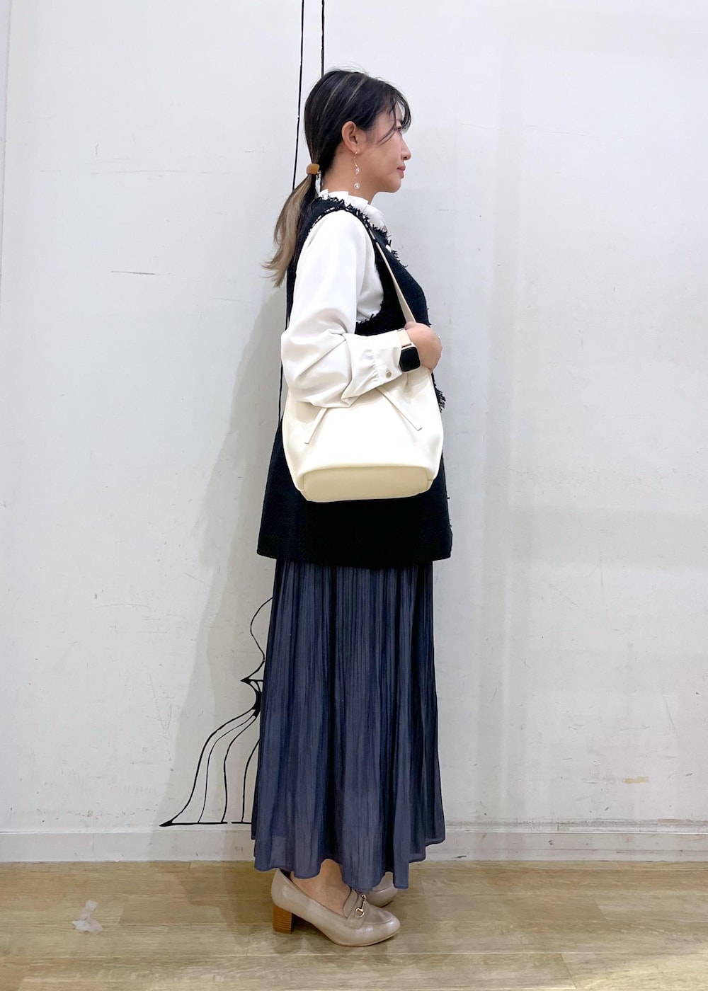 ブルー系のスカート、ベージュ系のローファー、ホワイト系のハンドバッグを着用したレディースの冬コーディネートの3枚目の写真