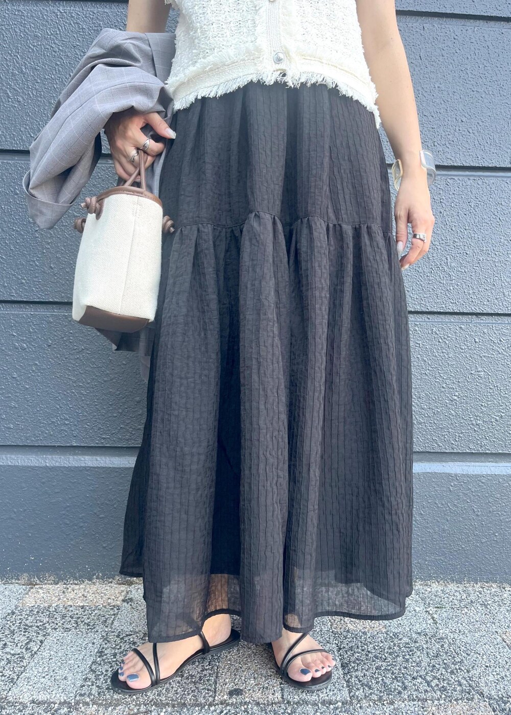 グレー系のテーラードジャケット、ブラウン系のトートバッグ、ブラック系のスカートを着用したレディースの夏コーディネートの6枚目の写真