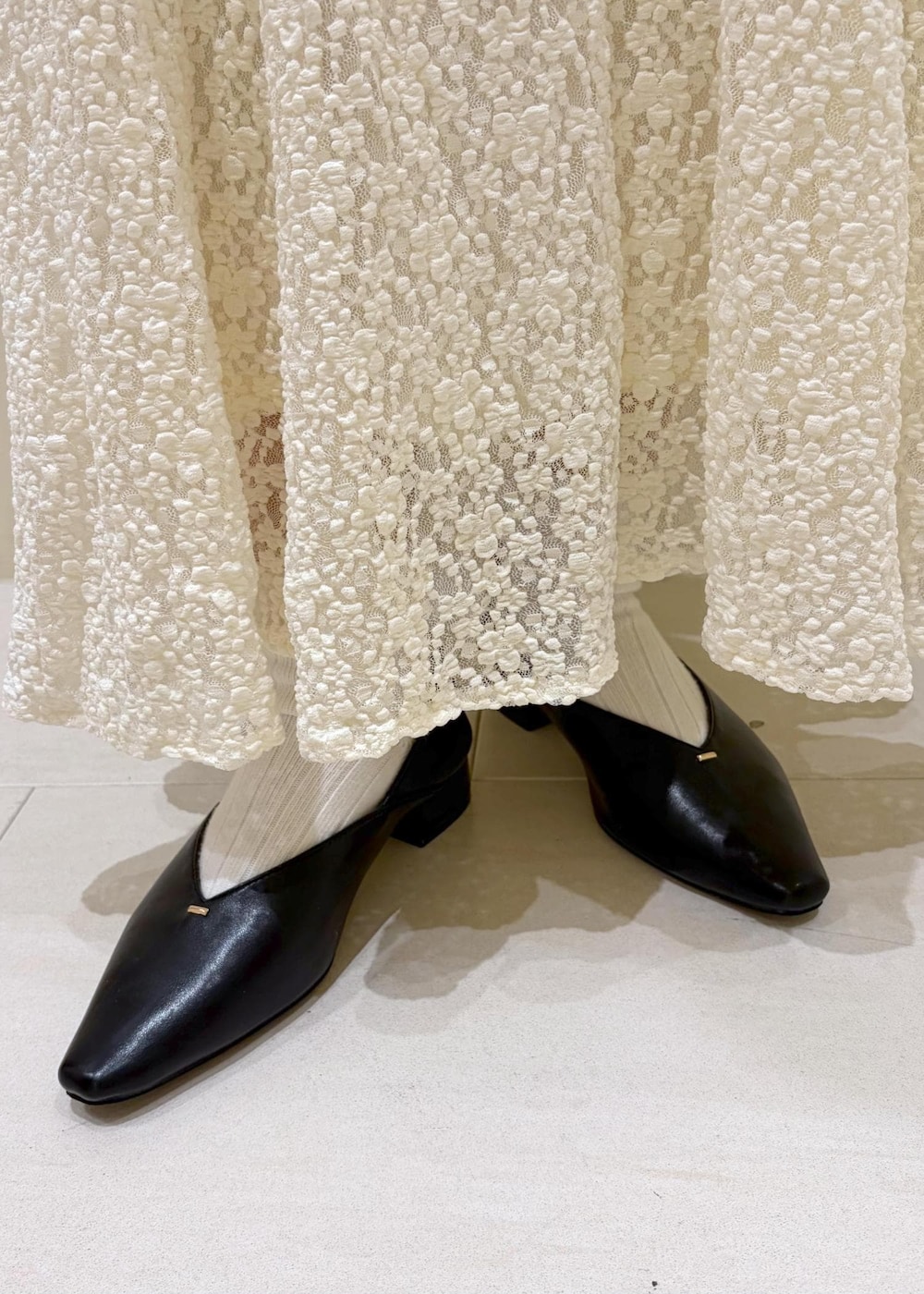 ブラック系のショルダーバッグ、ホワイト系のスカート、ホワイト系のカーディガン/ボレロを着用したレディースの冬コーディネートの9枚目の写真