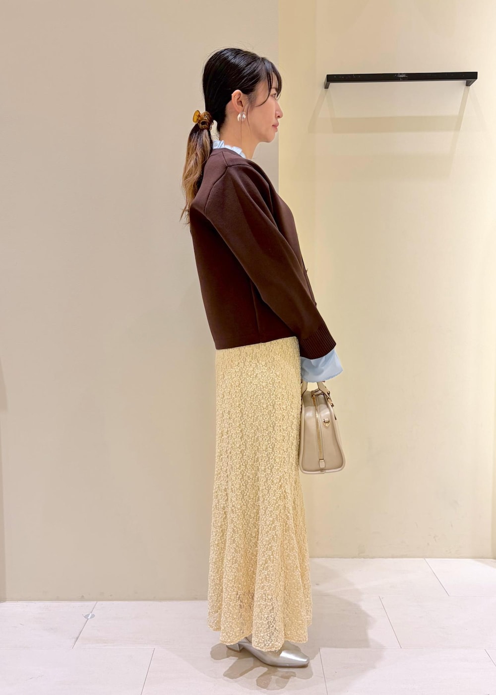 ホワイト系のボストンバッグ、ベージュ系のスカート、ブラウン系のカーディガン/ボレロを着用したレディースの春コーディネートの2枚目の写真