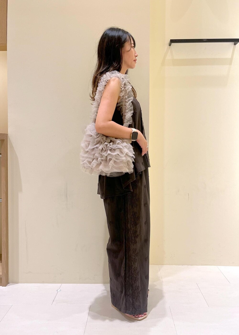 ベージュ系のショルダーバッグ、ゴールド系のサンダル、ブラック系のシャツ/ブラウスを着用したレディースの夏コーディネートの2枚目の写真