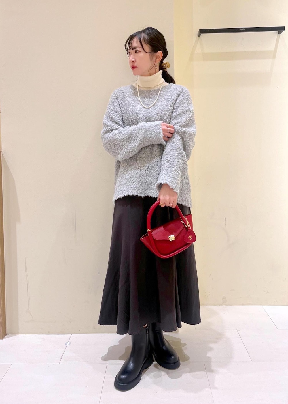 ホワイト系のニット/セーター、グレー系のスカート、レッド系のショルダーバッグを着用したレディースの冬コーディネートの2枚目の写真