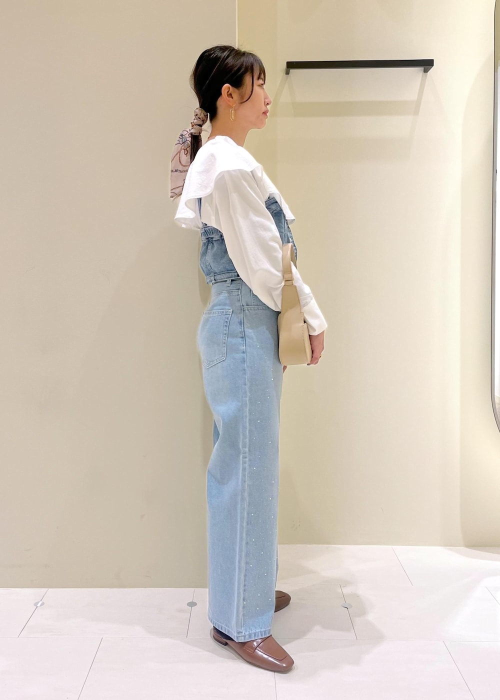 ベージュ系のハンドバッグ、ブルー系のデニムパンツ、ブルー系のベストを着用したレディースの春コーディネートの3枚目の写真