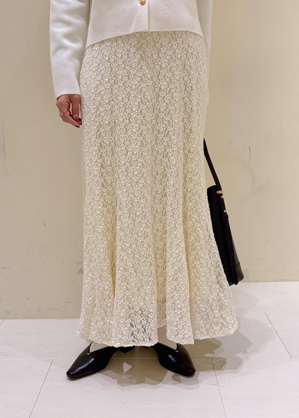 ブラック系のショルダーバッグ、ホワイト系のカーディガン/ボレロ、ホワイト系のスカートを着用したレディースの冬コーディネートの6枚目の写真