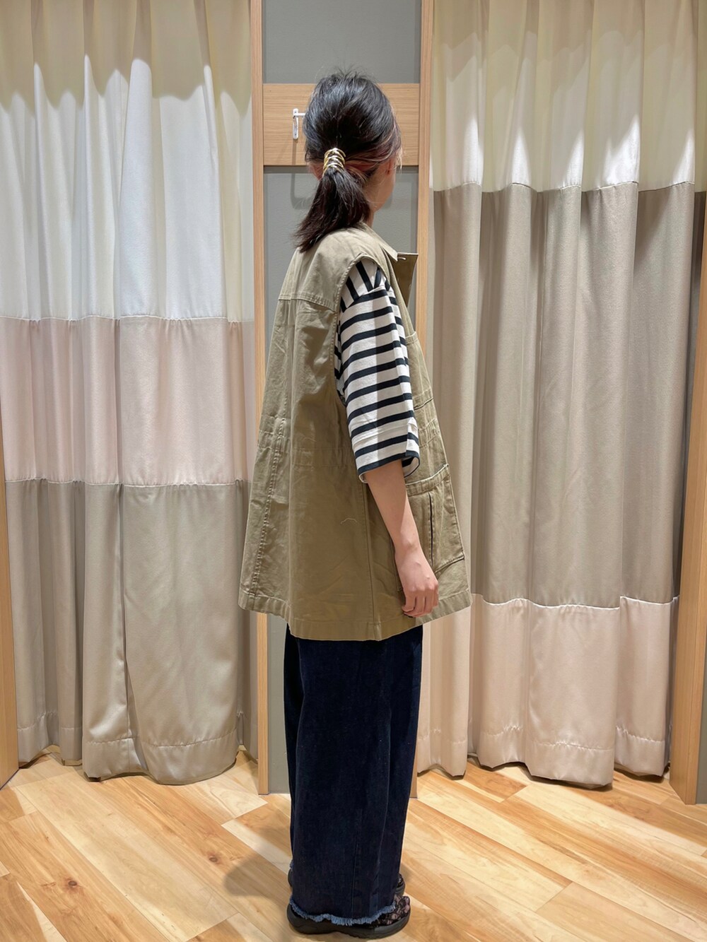 ベージュ系のベスト、グリーン系のTシャツ/カットソー、ブルー系のデニムパンツを着用したレディースの秋コーディネートの2枚目の写真