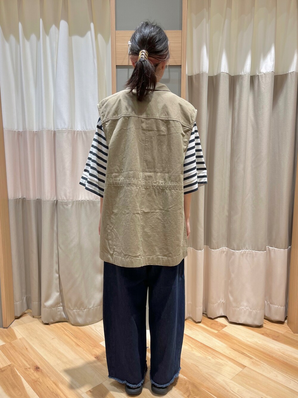 ベージュ系のベスト、グリーン系のTシャツ/カットソー、ブルー系のデニムパンツを着用したレディースの秋コーディネートの3枚目の写真